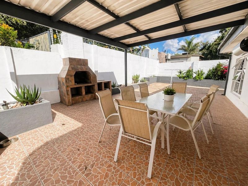A covered outdoor patio area featuring tiled flooring and a built-in brick braai, ideal for alfresco dining and entertaining.