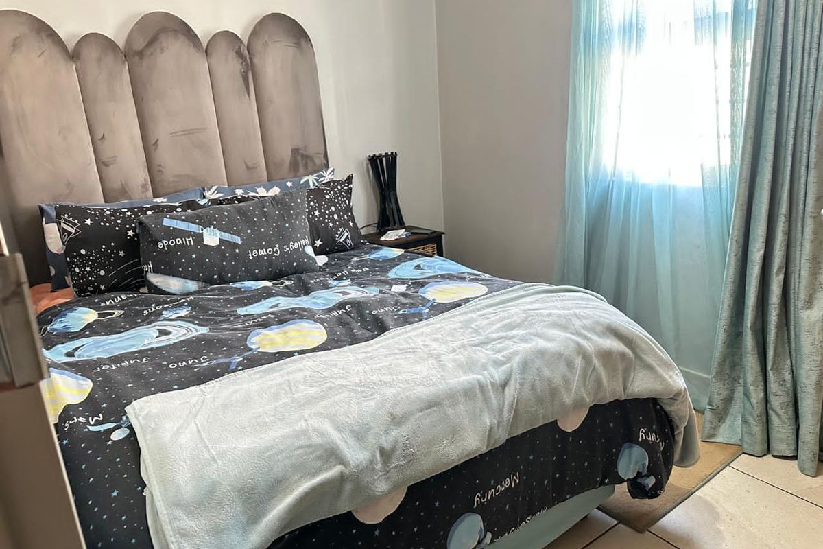 A functional bedroom featuring tiled flooring and a window with curtains, providing a comfortable and well-lit sleeping space.