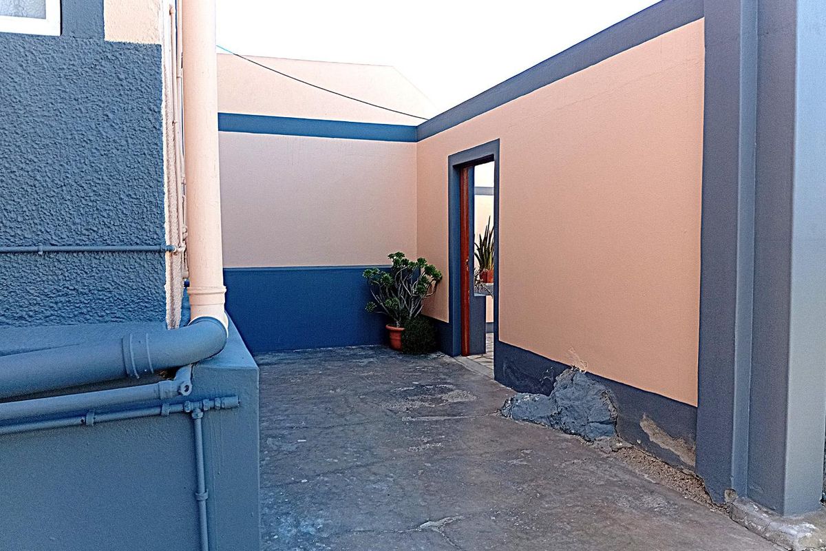 A rear exterior courtyard area featuring concrete paving and painted walls, showing signs of wear and structural weathering at the base.