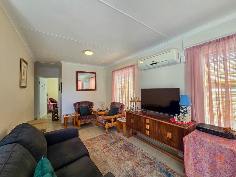 A comfortable living room featuring tiled flooring, a wall-mounted split-system air conditioner, and coved ceiling finishes.
