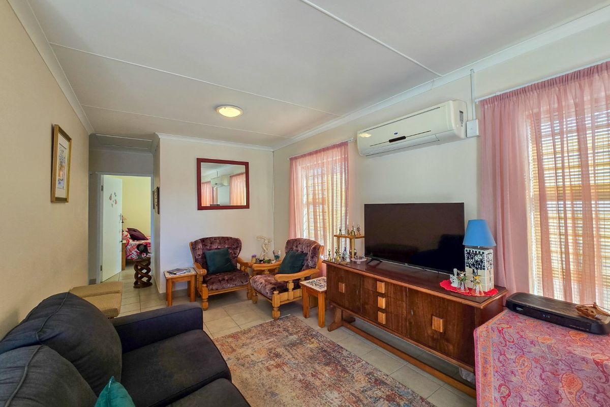 A comfortable living room featuring tiled flooring, a wall-mounted split-system air conditioner, and coved ceiling finishes.