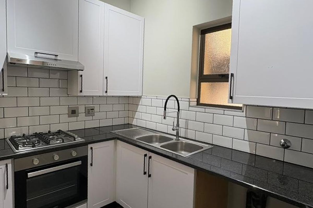 A clean, modern kitchen featuring white cabinetry, granite countertops, subway tile backsplash, and integrated gas hob and oven.
