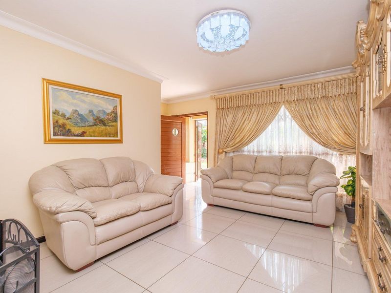 A well-maintained living room featuring neutral tiled flooring, cove cornicing, and a central decorative ceiling light fixture.