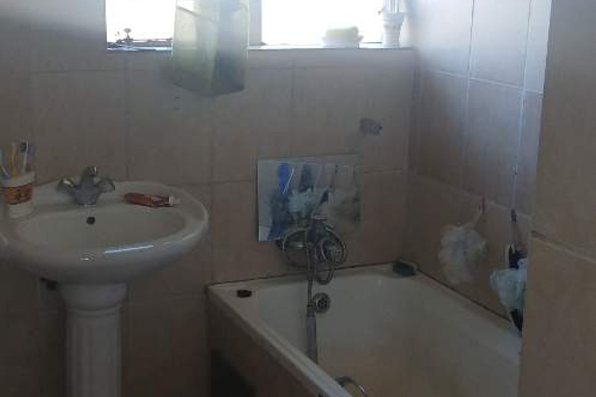 A functional bathroom featuring a pedestal basin and a built-in bathtub with tiled surrounds, requiring cosmetic updates to improve its overall condition.