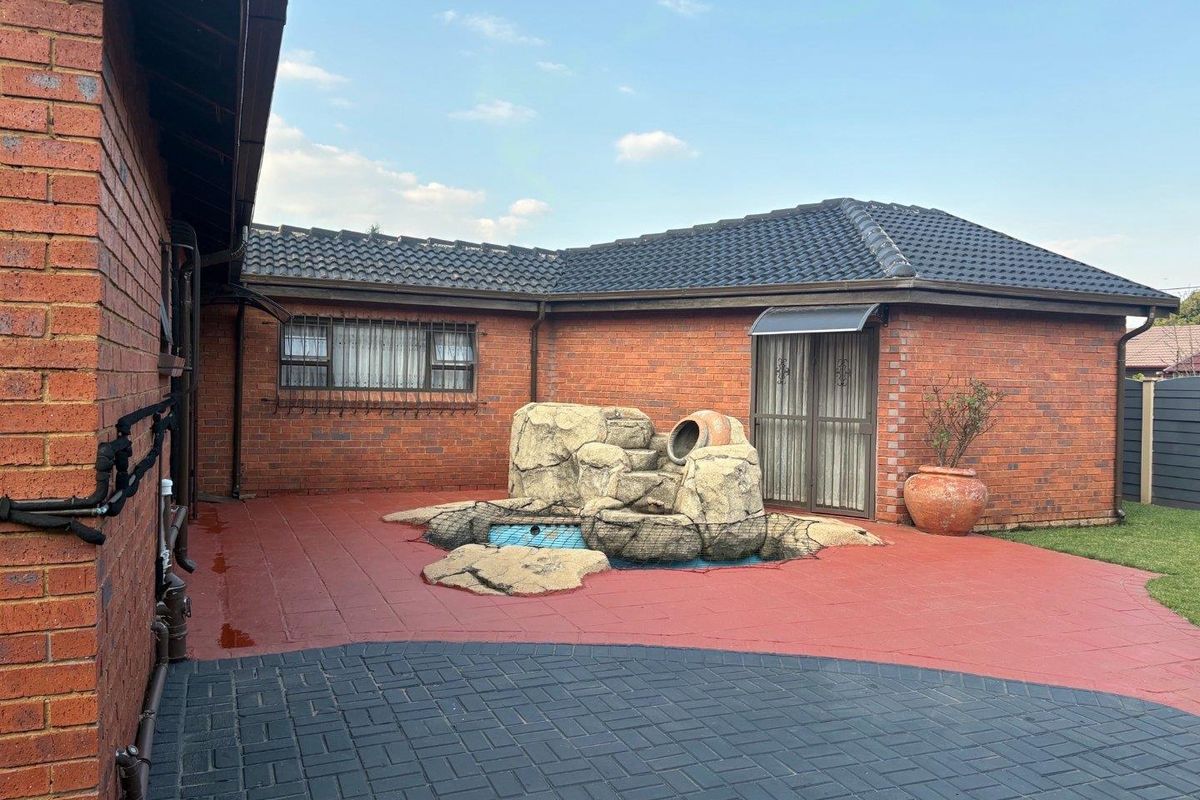 Rear exterior view of the cottage featuring a brick facade, tiled roof, paved patio area, and a decorative rock water feature.