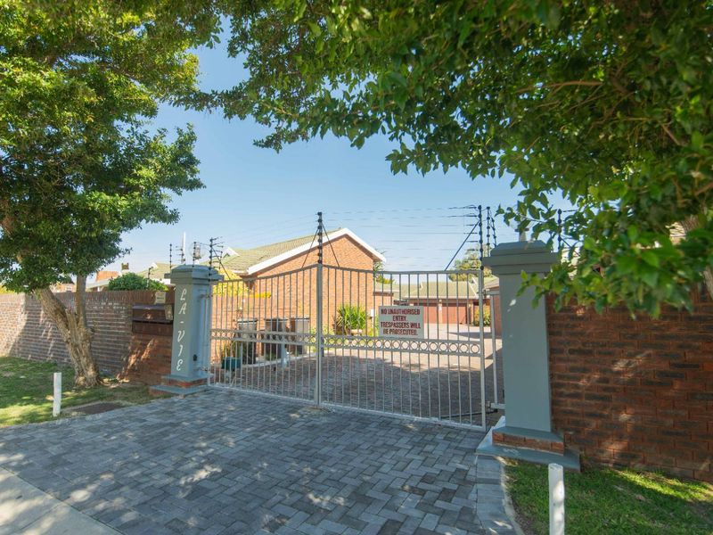 Front entrance view of the townhouse complex featuring a secure metal gate, brick boundary walls, and electric fencing.