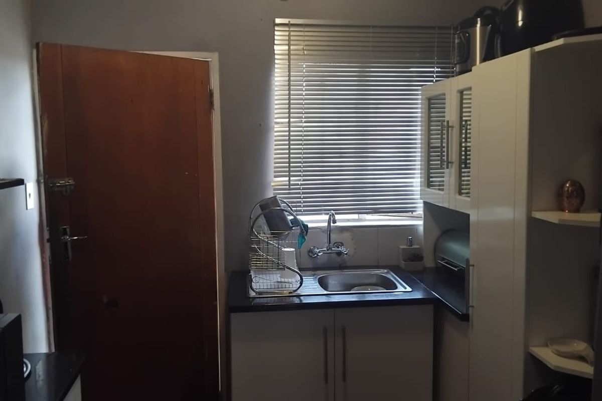 A compact kitchen area featuring built-in white cabinetry, a stainless steel sink, and a window with fitted blinds.