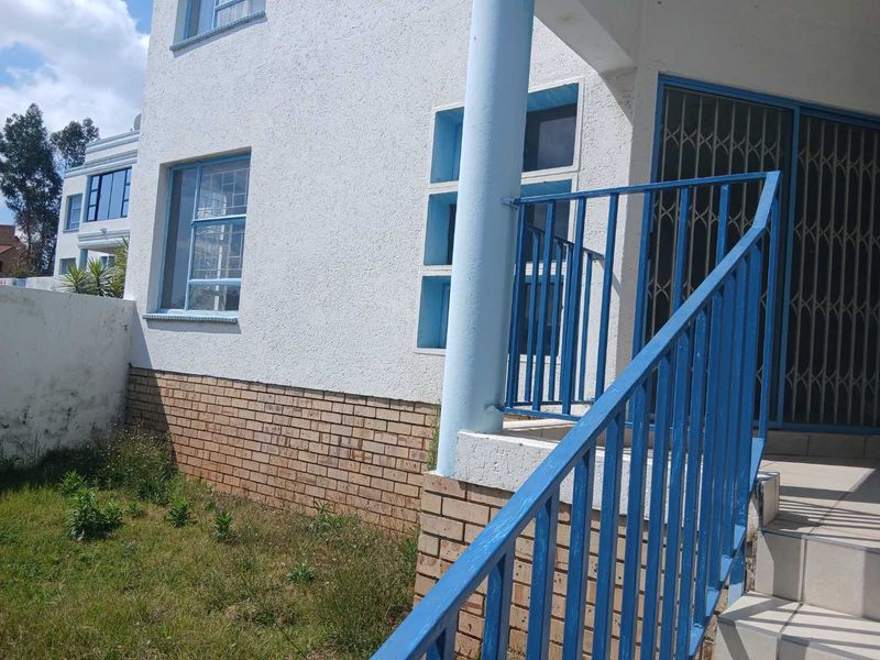 Front exterior view of a townhouse featuring a brick base, stucco facade, security gate, and metal staircase railing leading to the entrance.