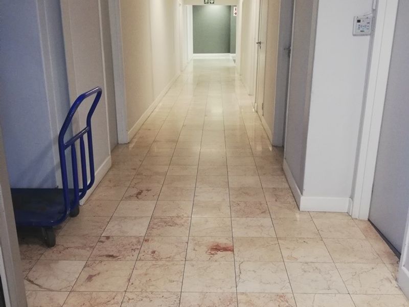 A long office hallway featuring tiled flooring, recessed ceiling lighting, and multiple access doors along the corridor.