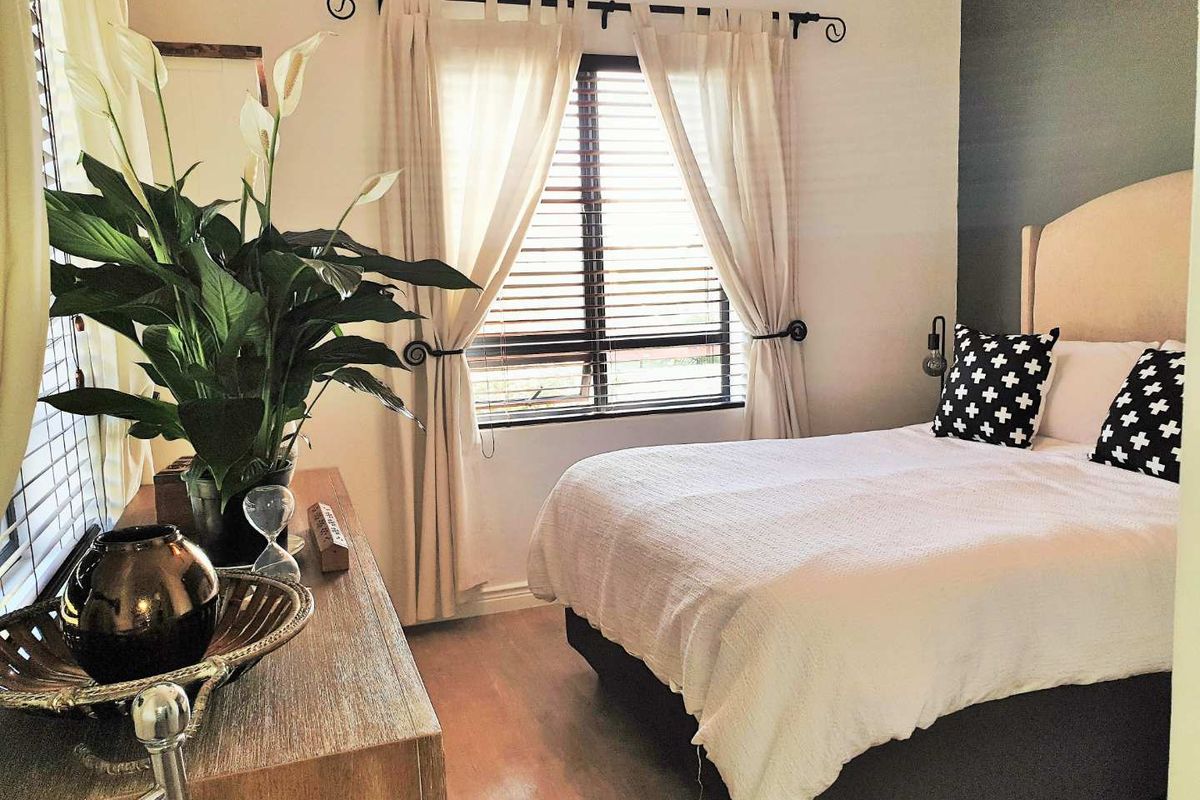 A well-lit bedroom featuring wood-look flooring, neutral wall tones, and a window fitted with horizontal blinds and decorative curtain rods.