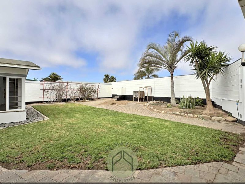 A rear garden area featuring a paved patio, lawn, and perimeter boundary walls, providing a private outdoor space.