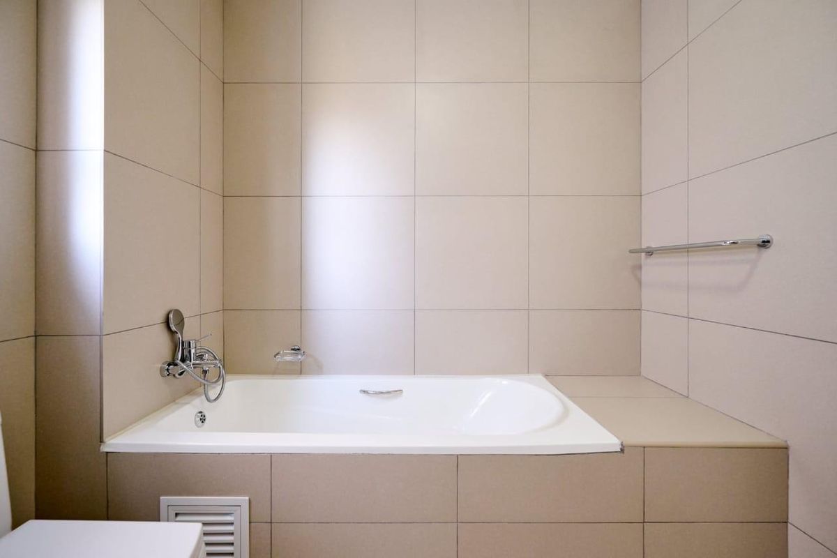 A clean, modern bathroom featuring a built-in bathtub with chrome fixtures and neutral wall tiling.