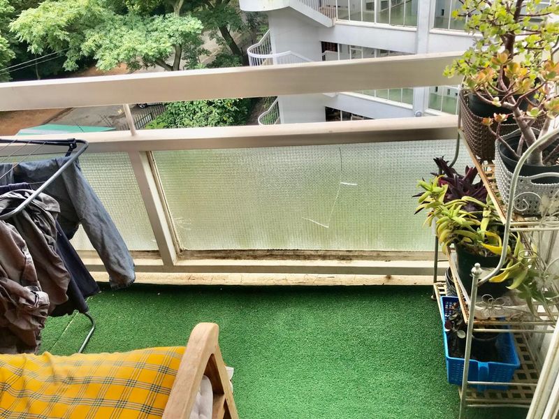 A balcony featuring artificial turf flooring, a metal railing, and a textured glass balustrade with visible damage.