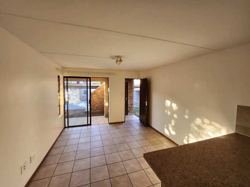 An empty open-plan living and kitchen area featuring tiled flooring, a sliding door leading to the exterior, and a built-in kitchen counter.