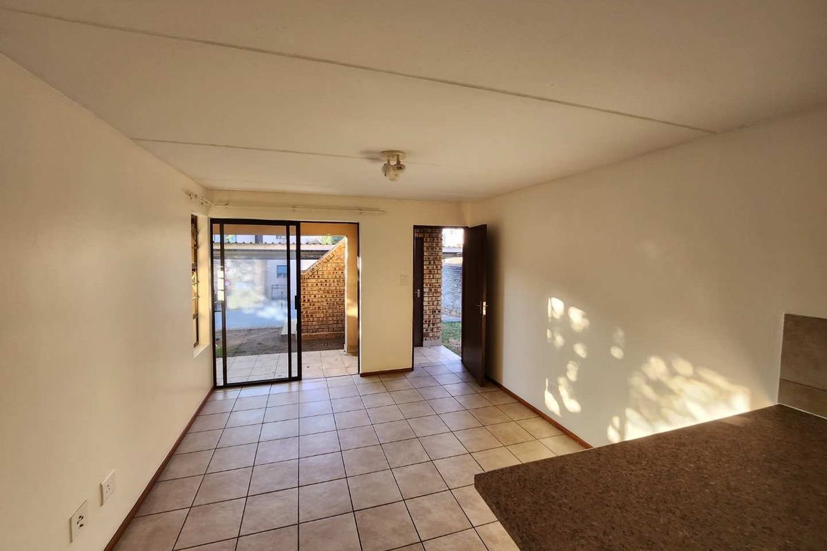 An empty open-plan living and kitchen area featuring tiled flooring, a sliding door leading to the exterior, and a built-in kitchen counter.