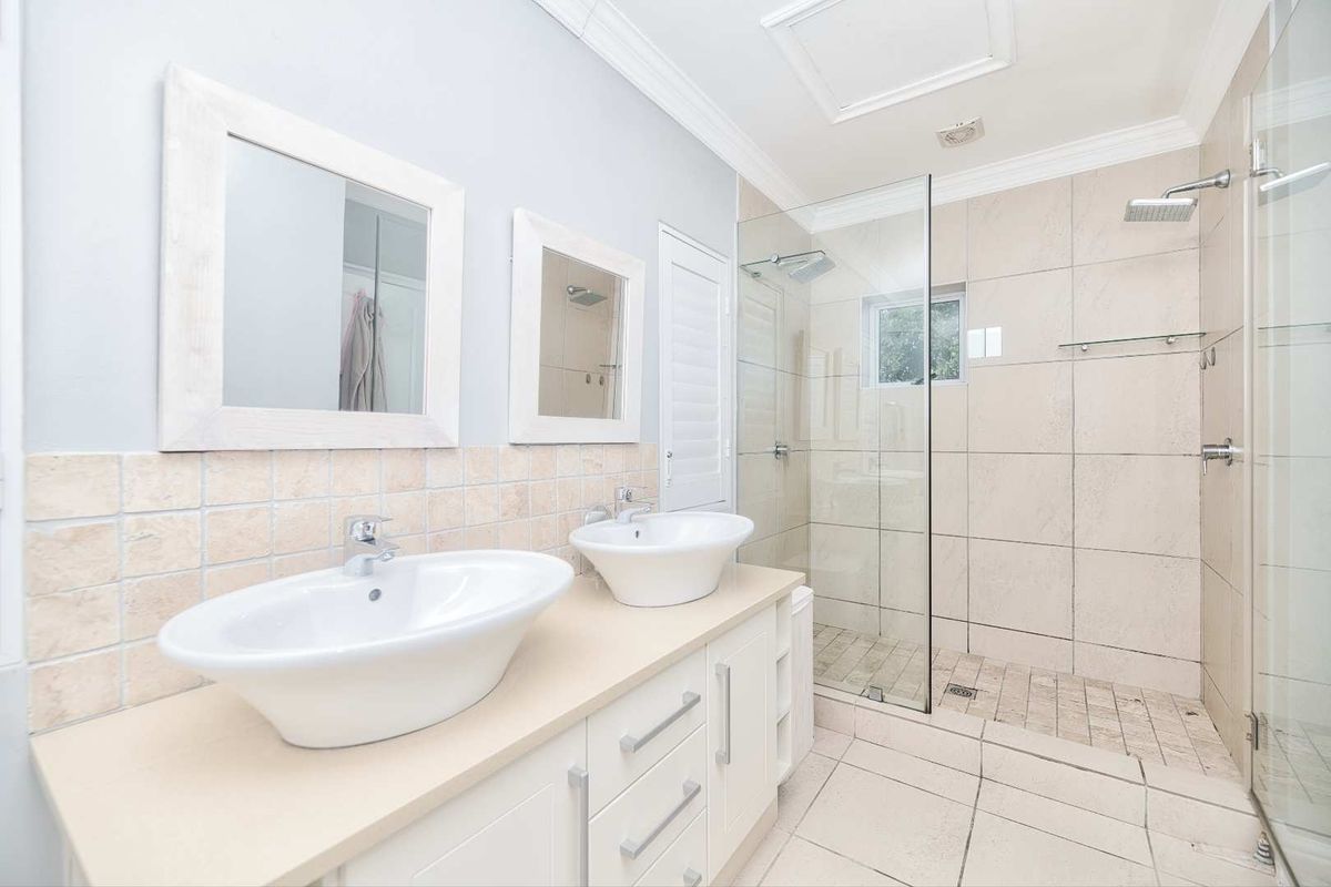 Modern bathroom featuring a double vanity with vessel sinks, a spacious walk-in shower with a glass screen, and neutral tiled finishes.