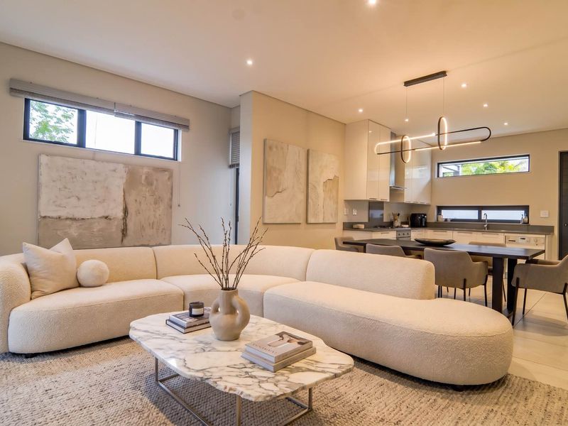 Modern open-plan living and kitchen area featuring sleek cabinetry, integrated appliances, recessed lighting, and neutral tiled flooring throughout.