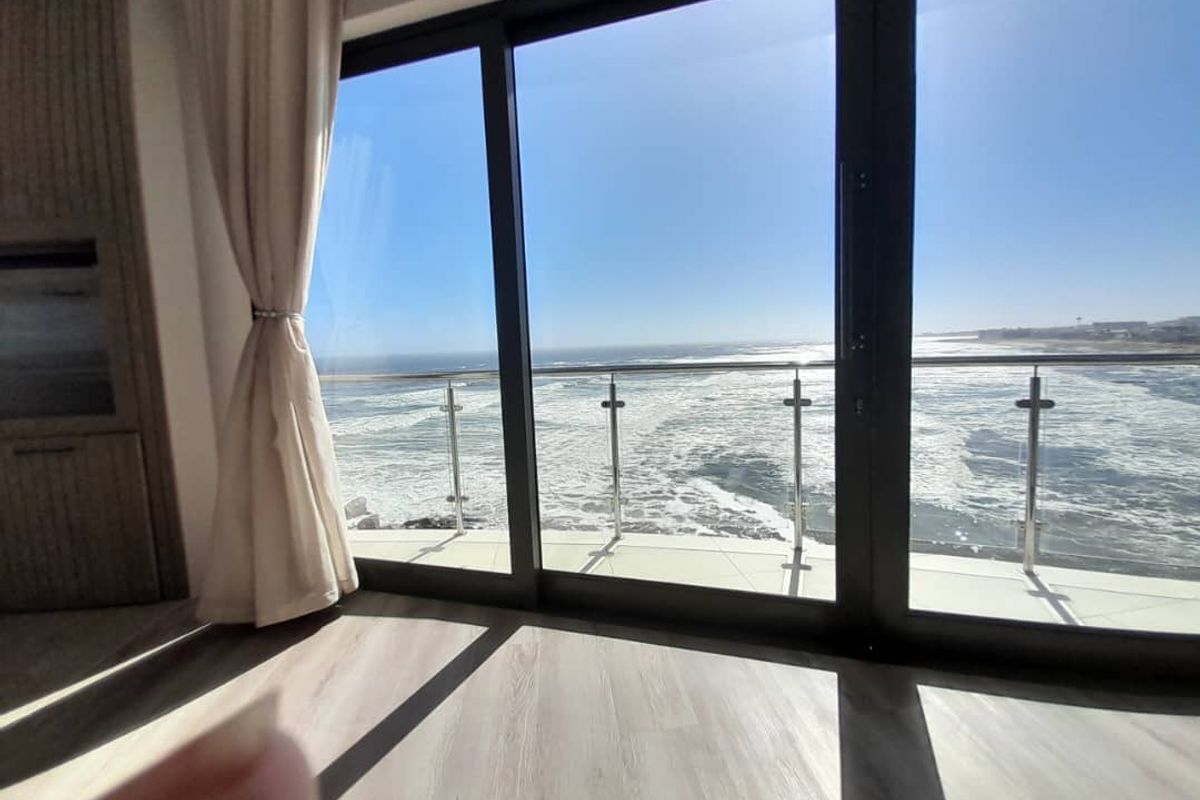 Modern bedroom featuring floor-to-ceiling sliding glass doors that open onto a private balcony with expansive, unobstructed ocean views.