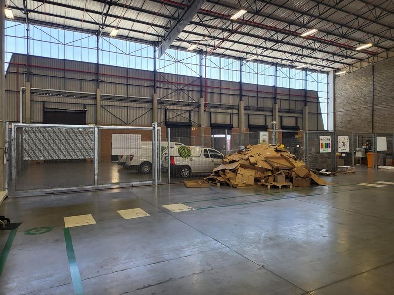 Spacious industrial warehouse interior featuring high ceilings, exposed steel trusses, concrete flooring, and secure internal fencing partitions.