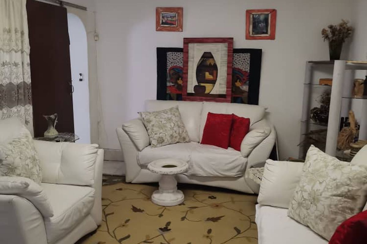 A living room space featuring basic finishes, fluorescent lighting, and access to an adjacent room through an arched doorway.