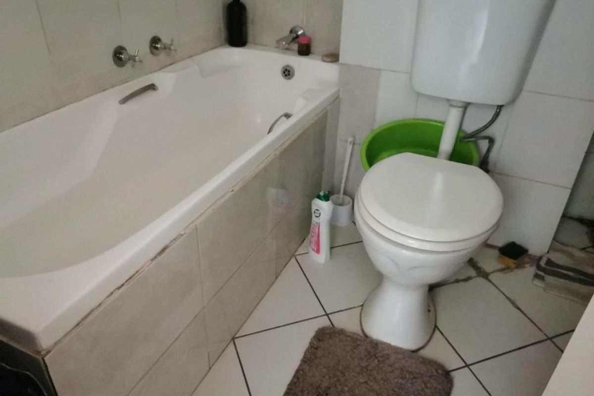 A compact bathroom featuring a built-in bathtub and toilet with tiled finishes, requiring some maintenance and cosmetic updates.