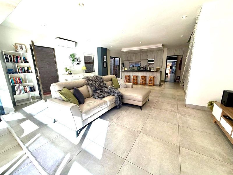 Open-plan living area featuring large format floor tiles, recessed ceiling lighting, and a modern kitchen with breakfast bar and built-in cabinetry.