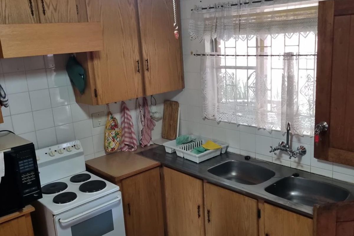 A functional kitchen featuring traditional wooden cabinetry, a double stainless steel sink, and a tiled backsplash with a window overlooking the exterior.