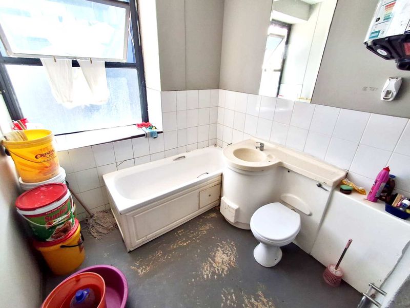 A dated bathroom featuring an integrated vanity unit, bathtub, and toilet, requiring cosmetic updates and flooring repairs to improve its overall condition.
