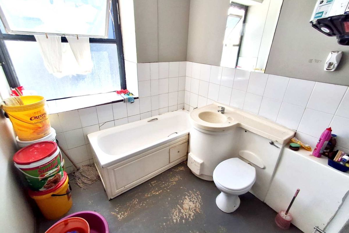 A dated bathroom featuring an integrated vanity unit, bathtub, and toilet, requiring cosmetic updates and flooring repairs to improve its overall condition.