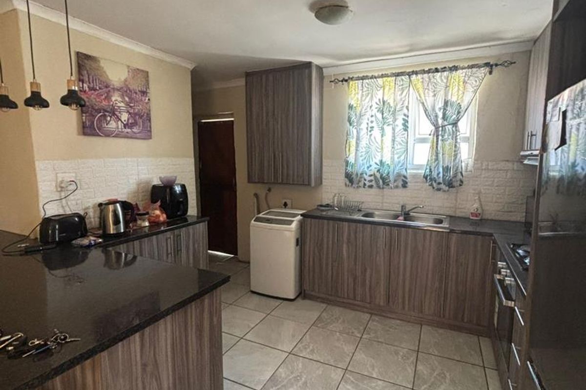 A functional kitchen featuring wood-grain cabinetry, dark granite countertops, tiled flooring, and a double-basin sink with integrated plumbing for laundry appliances.