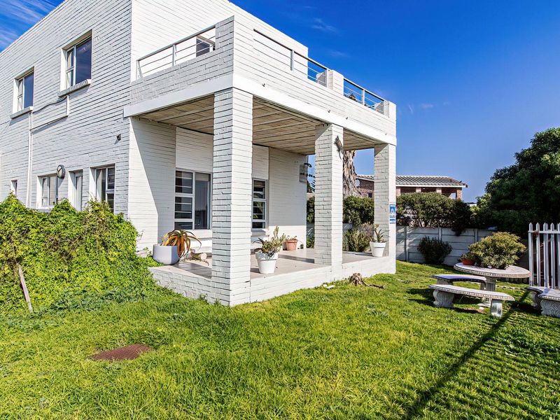 Rear view of a two-story white brick house featuring a covered ground-floor patio, an upper-level balcony with metal railings, and a surrounding garden area.