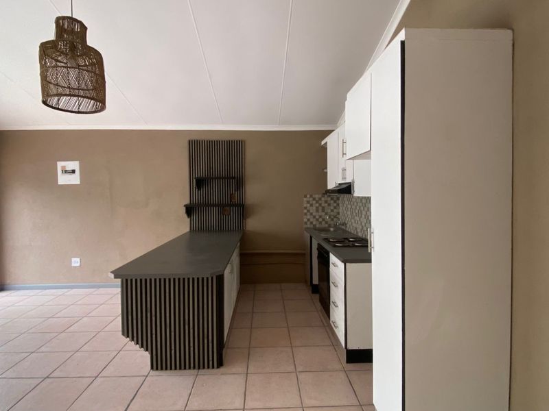 An open-plan kitchen area featuring a central island, built-in cabinetry, tiled flooring, and a neutral color palette, offering a functional layout for living and dining.