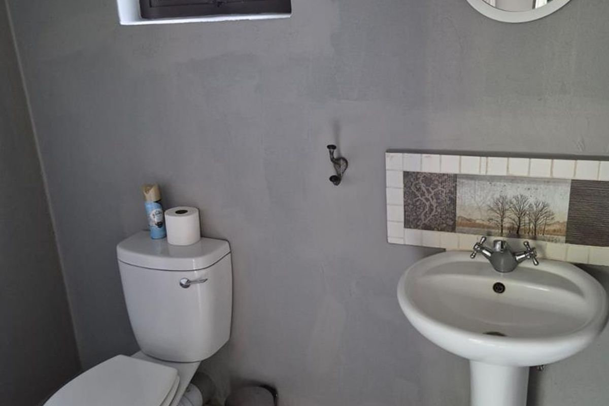 A functional bathroom featuring a pedestal basin with decorative tile backsplash, a standard toilet, and a small window for natural light.