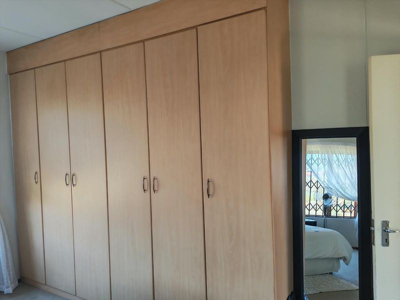 A bedroom featuring extensive floor-to-ceiling built-in wooden cupboards and a window fitted with a security gate.