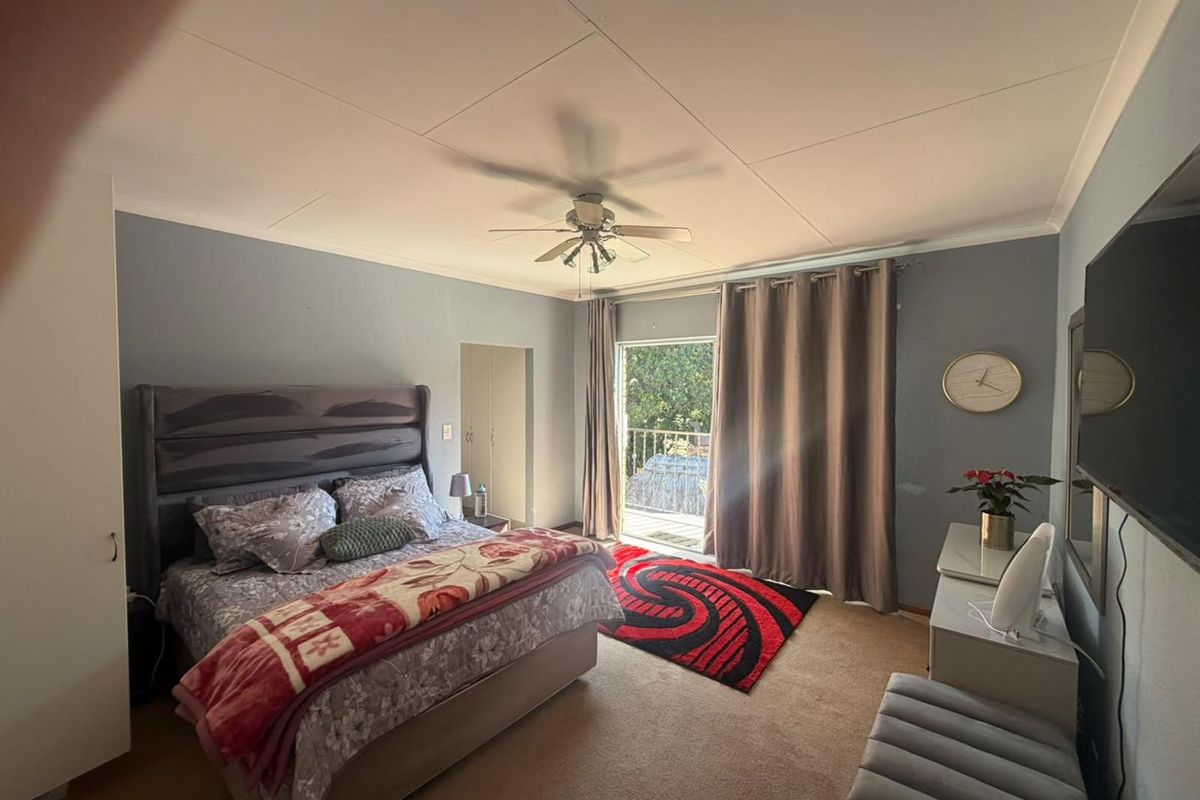 Spacious bedroom featuring neutral wall tones, a ceiling fan, built-in cupboards, and direct access to a private balcony through sliding glass doors.