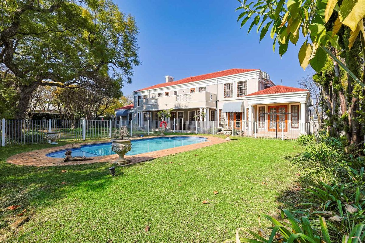 Rear view of a two-story residence featuring a swimming pool, manicured lawn, and a balcony overlooking the private garden area.