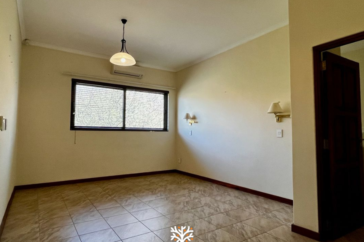 A spacious, empty bedroom featuring tiled flooring, a split-system air conditioner, and wall-mounted lighting, offering a neutral canvas for personalization.