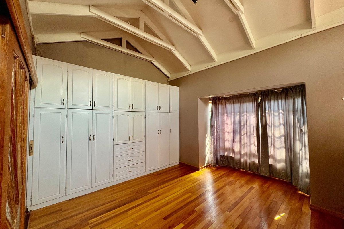A spacious bedroom featuring high vaulted ceilings with exposed beams, polished timber flooring, and extensive built-in cabinetry providing ample storage.
