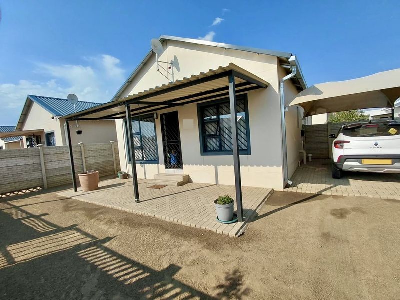 Front view of a residential house featuring a paved patio with a metal awning, security features, and an adjacent carport.