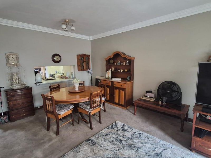 Open plan living and dining area featuring carpeted flooring, crown molding, and a convenient serving hatch connecting to the kitchen.