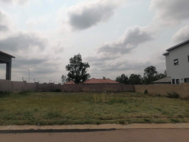 A vacant residential plot featuring a perimeter wall and street-side curb, offering a clear space ready for development.