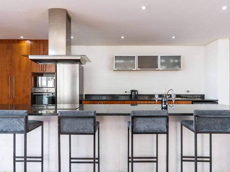 Modern kitchen featuring a large granite-topped island, stainless steel appliances, built-in oven, and ample wooden cabinetry with integrated lighting.