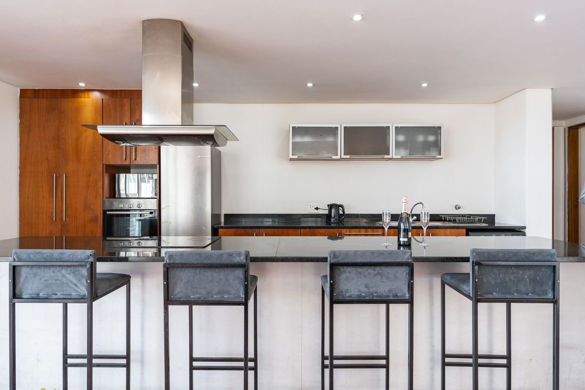 Modern kitchen featuring a large granite-topped island, stainless steel appliances, built-in oven, and ample wooden cabinetry with integrated lighting.