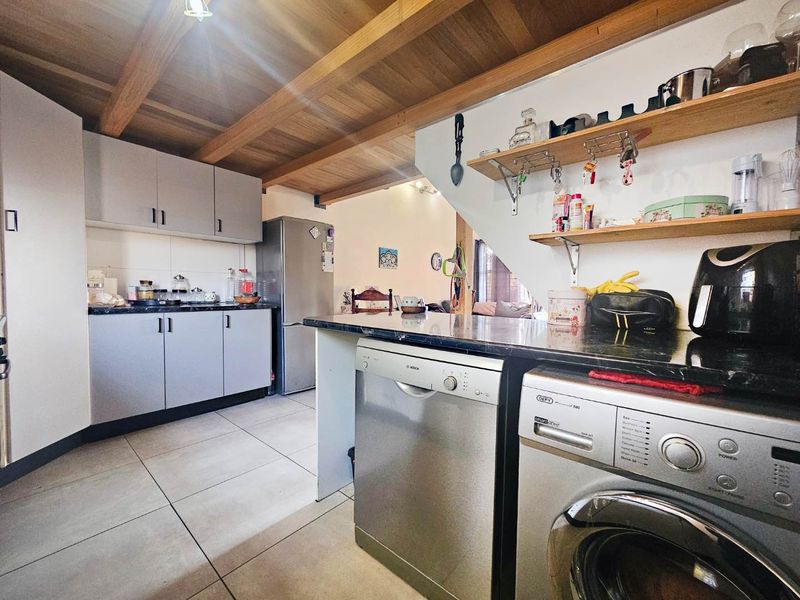 Functional kitchen featuring granite countertops, exposed timber ceiling beams, tiled flooring, and integrated laundry and dishwashing appliances.