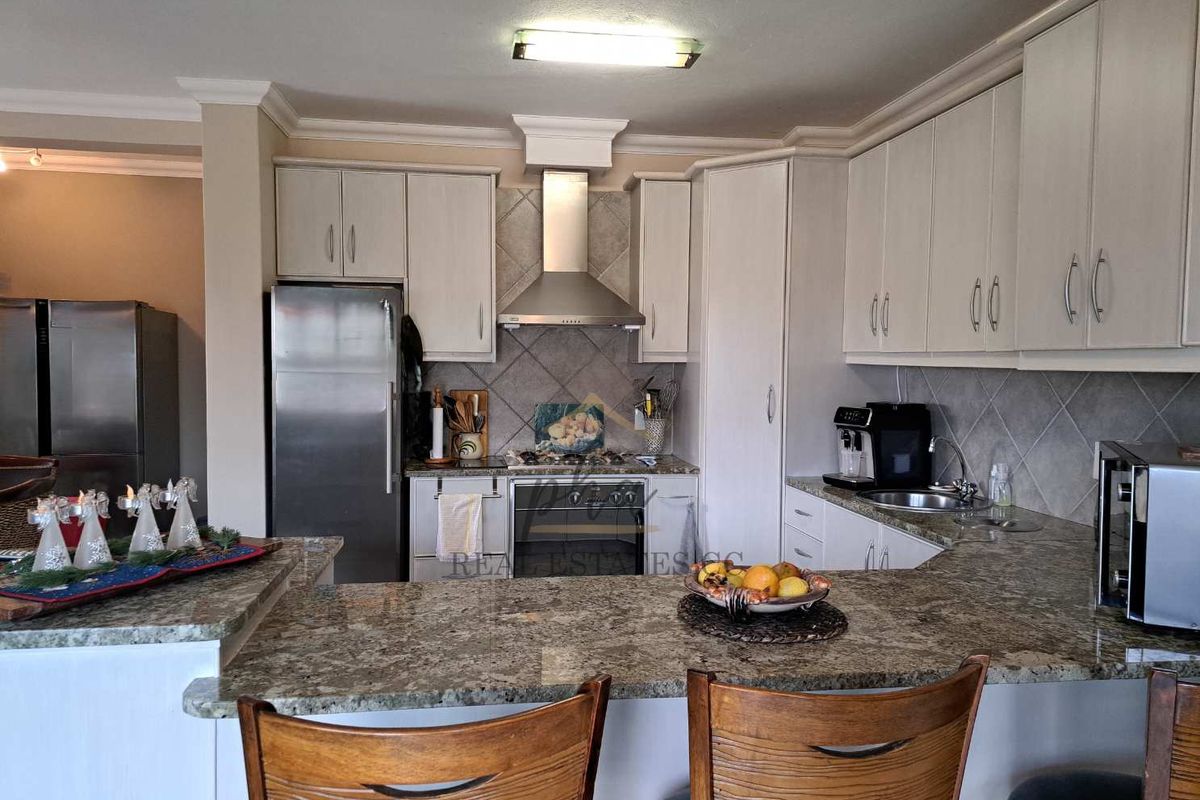 A functional kitchen featuring granite countertops, light-toned cabinetry, a built-in oven with extractor fan, and a breakfast bar peninsula.