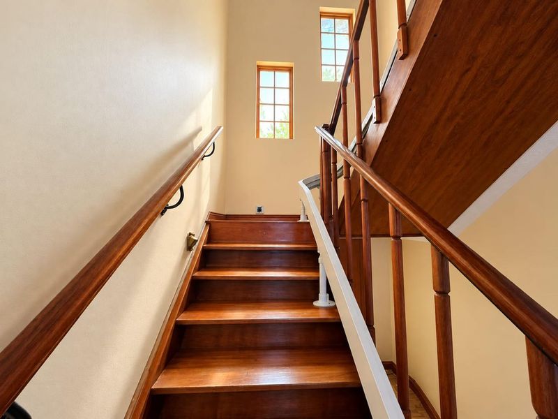 A well-maintained wooden staircase featuring a classic balustrade and handrail, illuminated by natural light from two small windows.