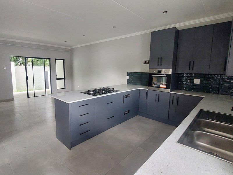 Modern open-plan kitchen featuring dark cabinetry, stone countertops, integrated gas hob, and built-in oven, flowing into a bright living area with sliding door access.