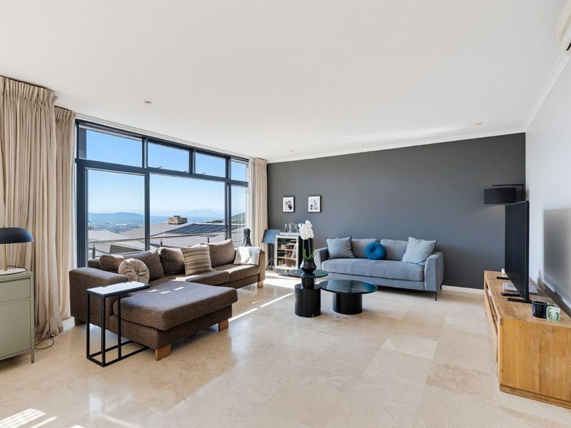 Spacious living room featuring large floor-to-ceiling windows with scenic views, elegant travertine tile flooring, and a modern dark feature wall.