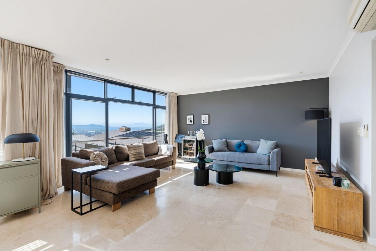 Spacious living room featuring large floor-to-ceiling windows with scenic views, elegant travertine tile flooring, and a modern dark feature wall.