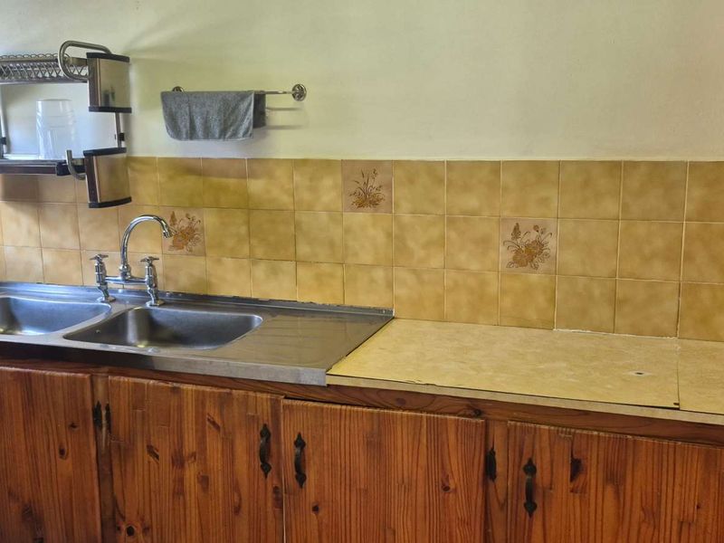 A functional kitchen area featuring traditional wooden cabinetry, a double stainless steel sink, and a tiled backsplash with a laminate countertop.